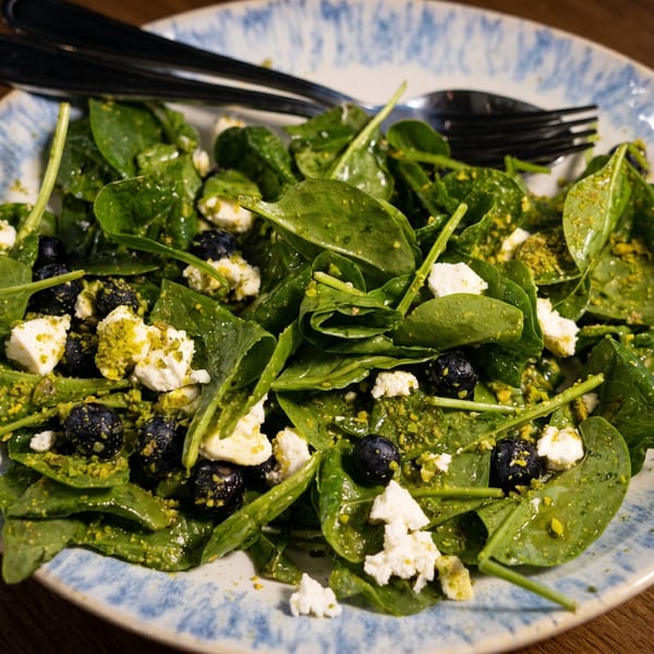 Spinach salad with blueberries, feta cheese, and pistachio crumbles on a blue and white plate.