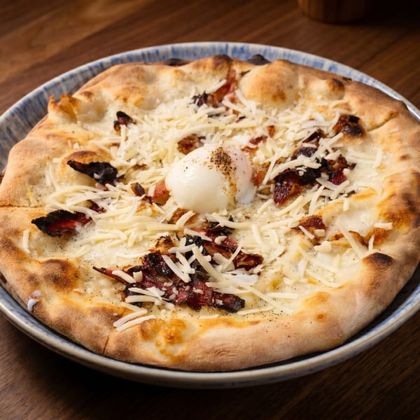 A white pizza with bacon, shredded cheese, and a poached egg on a blue and white plate.