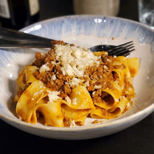 Close-up of pappardelle pasta with rich bolognese sauce and grated cheese in a blue and white bowl.