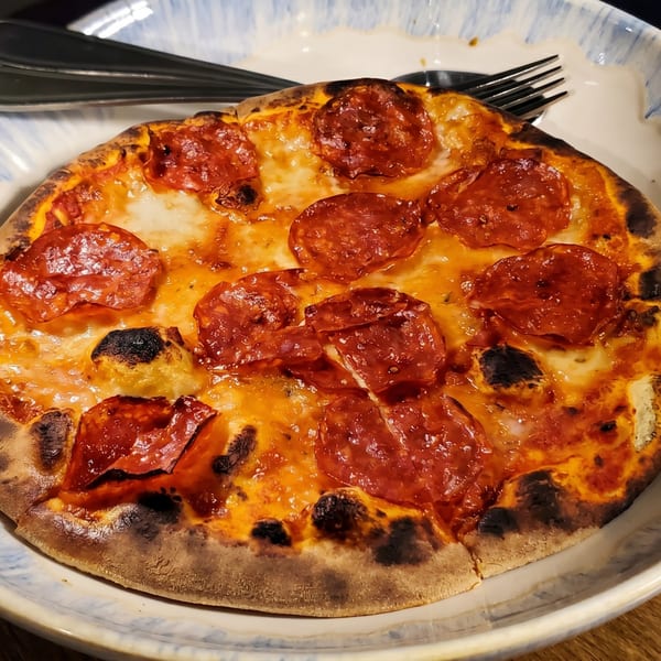 A close-up of a pepperoni pizza with a crispy crust, served on a white and blue plate.